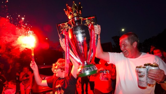Los fanáticos del Liverpool sostienen una réplica del trofeo de la Premier League mientras celebran la victoria del título de su equipo.  AP
